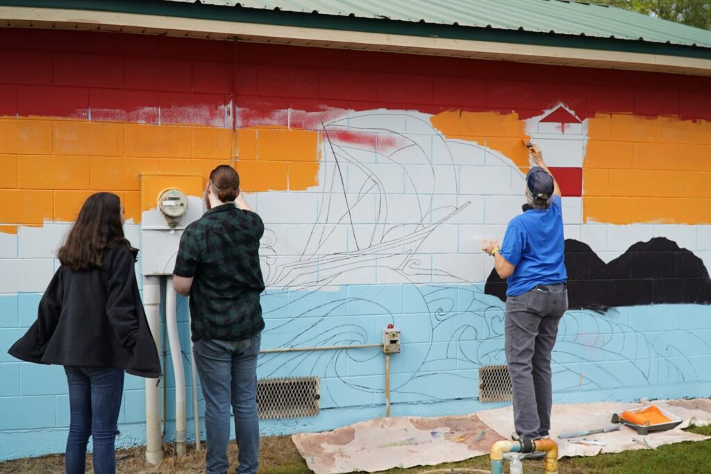 adults painting mural on side of building